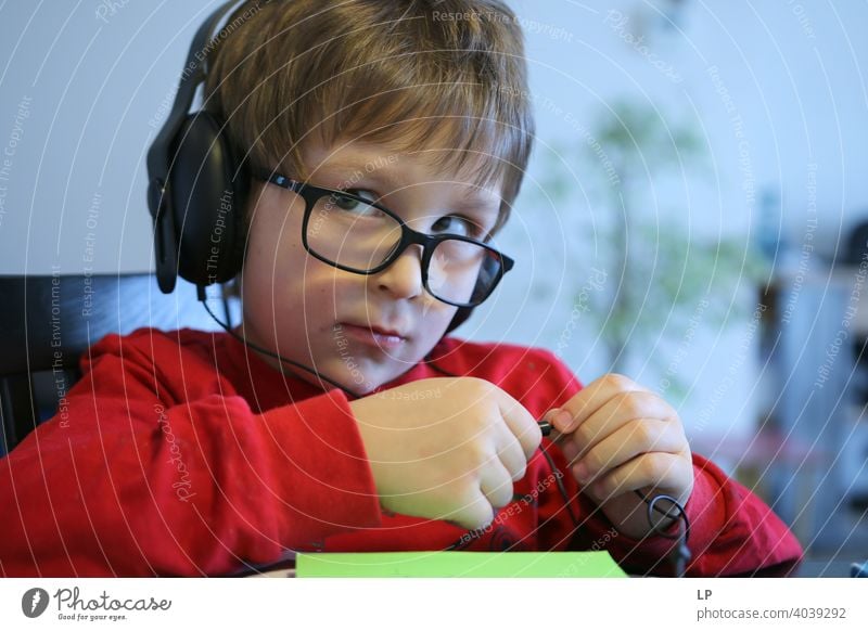 Kind mit Brille und Kopfhörer schaut sehr ernst von der Kamera weg skeptisch Zweifel Unsicherheit Kindheit Realität Experiment Hintergrundbild Idee abstrakt