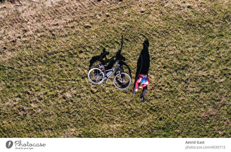 Luftaufnahme mit einer Drohne von einer Fahrradfahrerin mit Rad auf einer Wiese mit Licht und Schatten luftaufnahme drohnenfoto frühling sport radfahren fahrrad