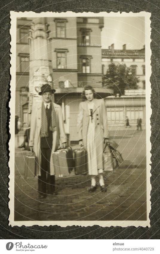Schwarz-Weiß-Foto mit Büttenrand aus den 1950er Jahren auf einer schwarzen Fotoalbumseite, ein junges Paar mit Reisekoffern zeigend / Urlaubsreise / Erinnerungen / analoge Fotografie