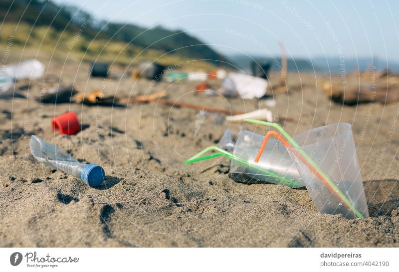 Schmutzige Strandlandschaft voller Müll Strohhalme Einwegbecher Kunststoff kontaminiert Sand dreckig Umwelt Natur Verschmutzung Abfall Küste Kunststoffdeckel