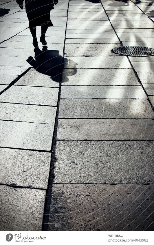 Läuft. Schatten Mensch Person Frau Seniorin gehen Licht und Schatten Boulevard Gehwegplatten Fußgängerzone allein Gullydeckel Spaziergang Erwachsene laufen