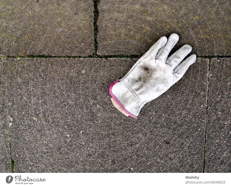 Verschmutzter weißer Arbeitshandschuh auf grauen Steinplatten in Oerlinghausen bei Bielefeld im Teutoburger Wald in Ostwestfalen-Lippe Handschuh Fingerhandschuh