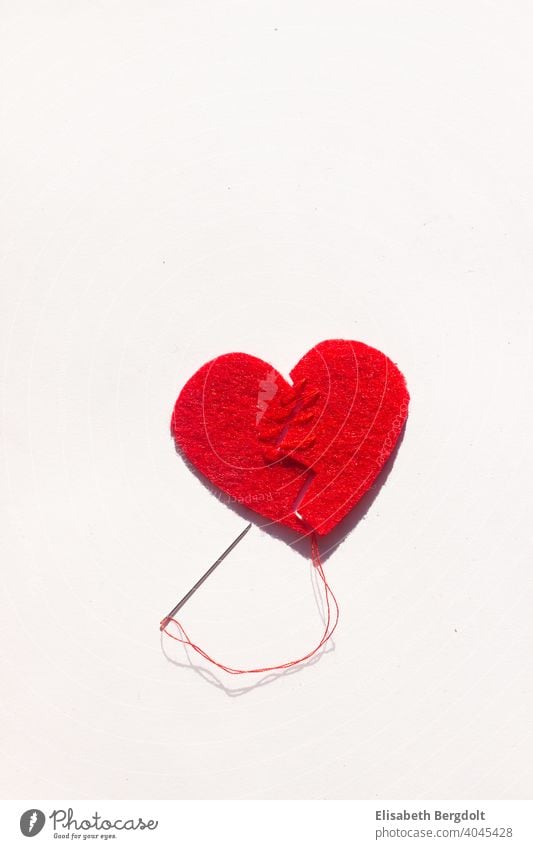 gebrochenes rotes Herz (aus Filz) auf weißem Hintergrund, das mit Nadel und Faden wieder zusammengenäht wird Liebeskummer gebrochenes Herz Herzschmerz
