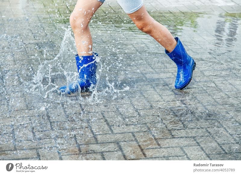 Mädchen in blauen Gummistiefeln springt in eine Pfütze nach einem Regen Herbst Stiefel Wasser Saison nass Wetter Spaziergang Spaß Kind im Freien Beine Straße