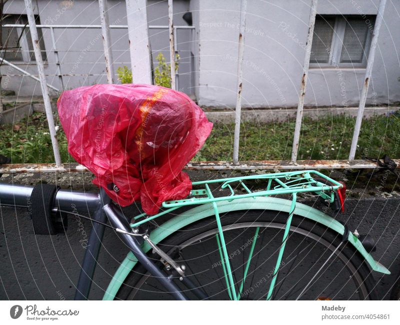 Fahrrad in Grau und Türkis mit transparenter roter Plastiktüte über dem Sattel vor einem alten Eisenzaun im Nordend von Frankfurt am Main in Hessen Rad Stadtrad