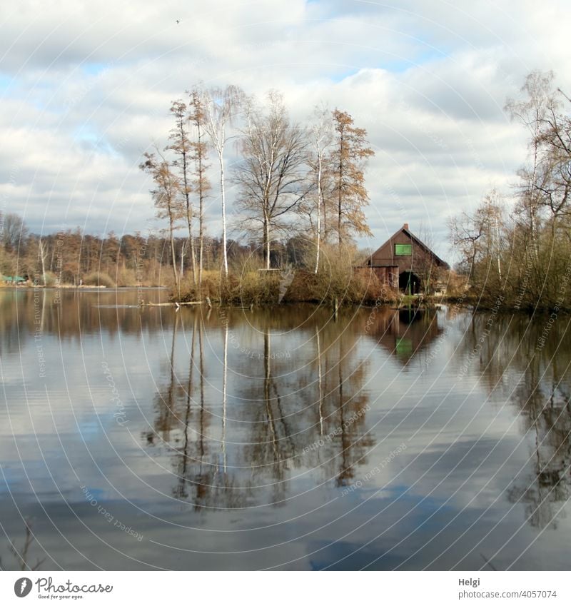 alte Holzhütte am See mit Bäumen , Wolken am Himmel und Spiegelung im Wasser Haus Hütte Gebäude Moorsee Winter Reflexion & Spiegelung Menschenleer Landschaft