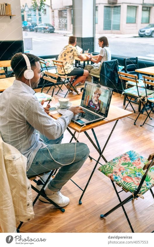 Mann spricht per Videoanruf mit seiner Mutter sprechend Laptop Kaffeehaus Internet Kopfhörer Bildschirm Videokonferenz männlich Café Tisch Familie