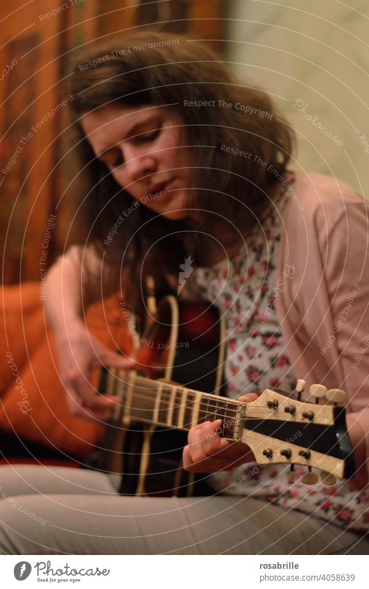 versunken ins Gitarrenspiel - junge brünette Frau sitzt zuhause auf dem Sofa und spielt Gitarre Musik Musikerin spielen musizieren Kunst Kleinkunst