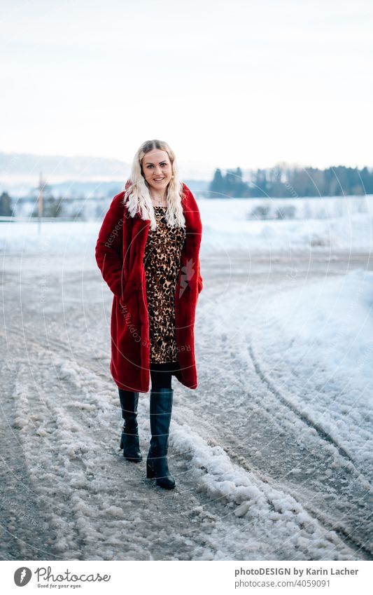 junge Frau 30 Jahre im Schnee mit rotem Mantel und Leopardenkleid blonde Haare Locken Freude Hoffnungsvoll Strasse, schwarze Stiefel Fashion Kleid leopard Model