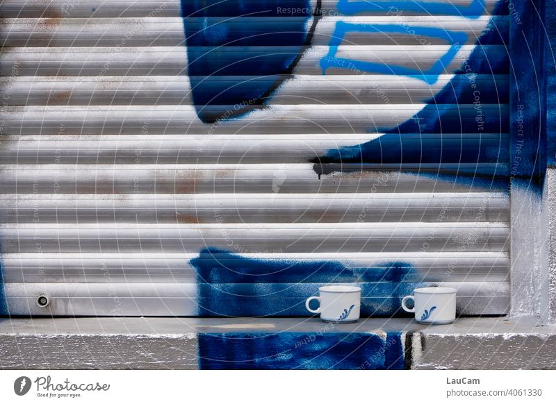 Zwei Tassen auf einer Fensterbank vor geschlossenem Rolladen mit silber-blauem Graffiti Rollladen Rollo weiß silbern Kaffee Kaffeetasse Kaffeetassen