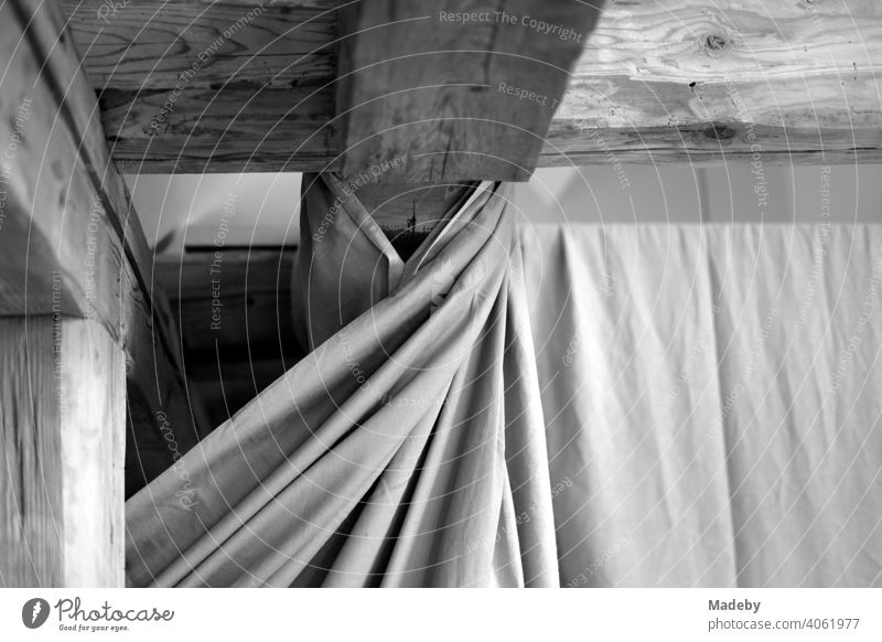 Schöne alte Dachbalken aus Holz unter dem Dach und Vorhang mit Falten in einem renovierten Bauernhaus auf einem Bauernhof in Rudersau bei Rottenbuch im Kreis Weilheim-Schongau in Oberbayern, fotografiert in klassischem Schwarzweiß