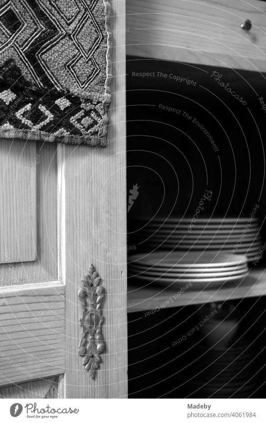 Weiße Teller auf dem Regalboden eines alten Bauernschrank aus massivem Holz im Wohnzimmer eines alten Bauernhaus in Rudersau bei Rottenbuch im Kreis Weilheim-Schongau in Oberbayern, fotografiert in neorealistischem Schwarzweiß