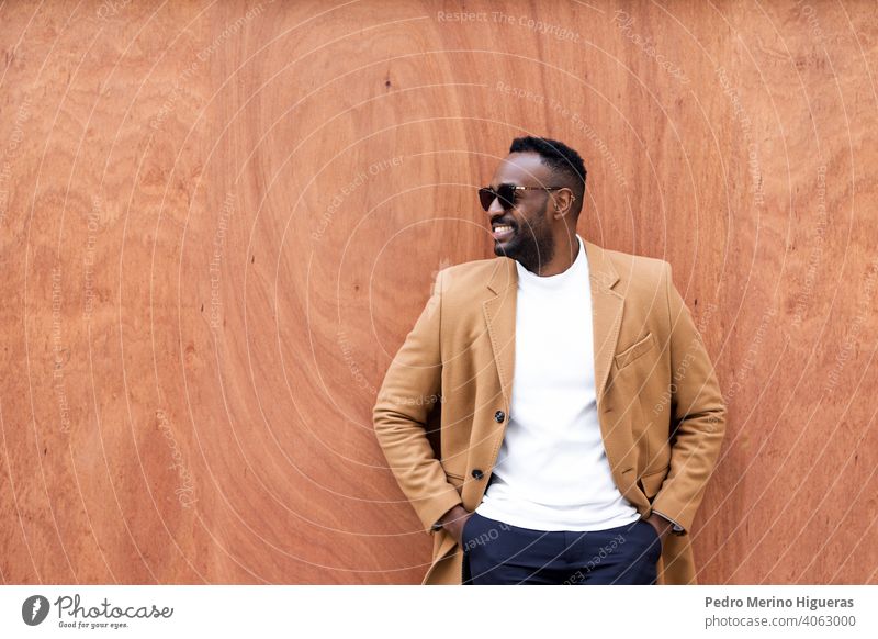 Gutaussehender schwarzer Mann, der an einer Wand lehnt und lächelnd zur Seite schaut. Afrikanisch Sonnenbrille Freizeit schreibend Porträt Großstadt urban