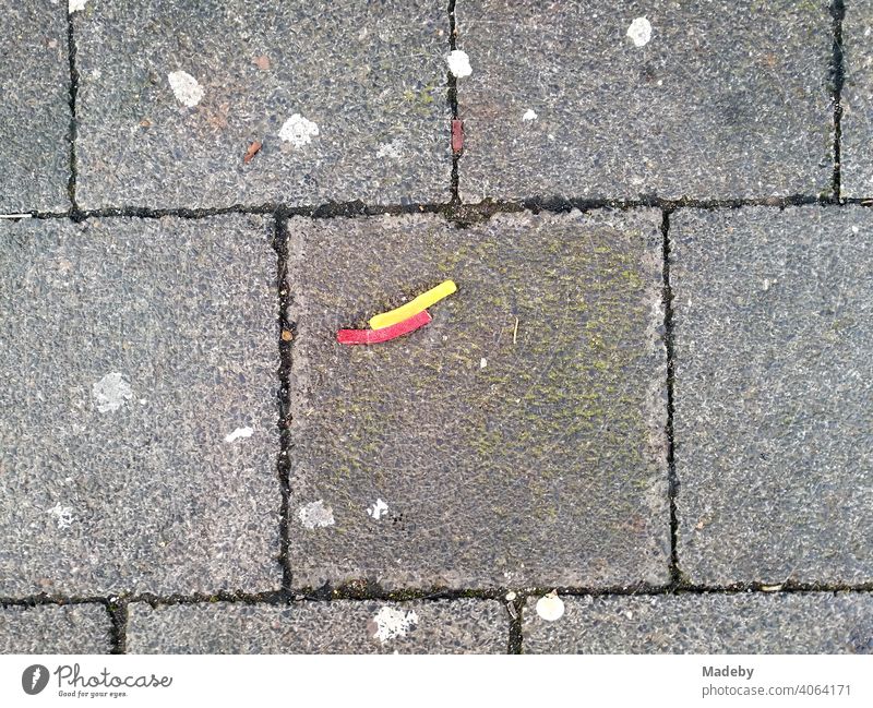 Lakritzstreifen in Gelb und Rot auf grauen Steinplatten mit Kaugummiresten auf einem Platz in Offenbach am Main in Hessen verrotten gelb künstlich Korkenzieher
