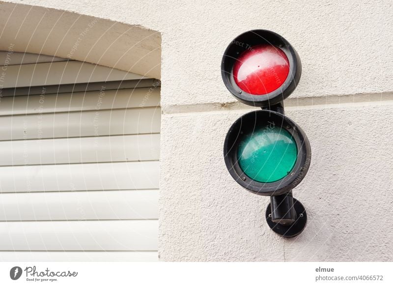 kleine rote und grüne Signallampen an der Hauswand neben einer geschlossenen Garageneinfahrt mit Rolltor / Ampel Ampelverkehr Einfahrt Hauseinfahrt Gebäude