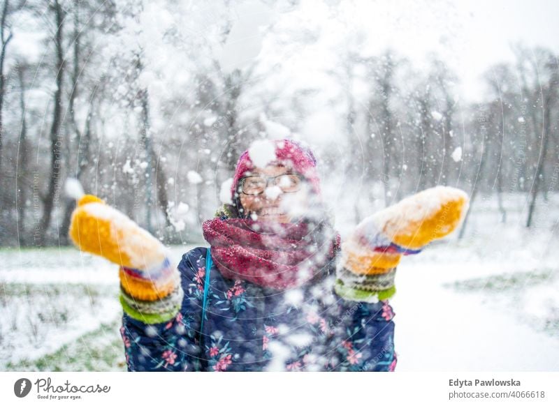 Frau wirft Schnee in die Luft und genießt einen kalten Wintertag Werfen Brille außerhalb natürlich Gesundheit Fausthandschuh Schal Bäume Handschuhe Schneeflocke