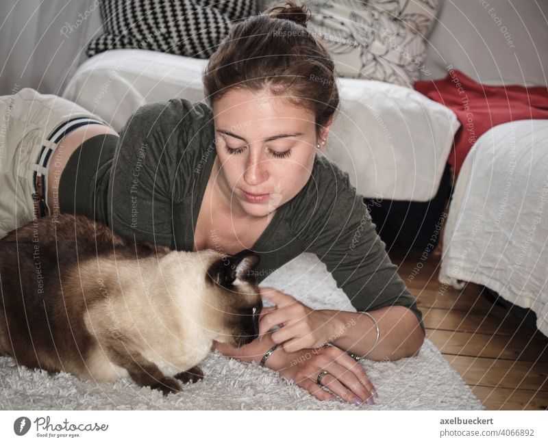 Junge Frau krault ihre Siamkatze auf dem Boden liegend Katze Haustier gemütlich zu Hause Kraulen Streicheln kuscheln Lifestyle entspannend Erholung