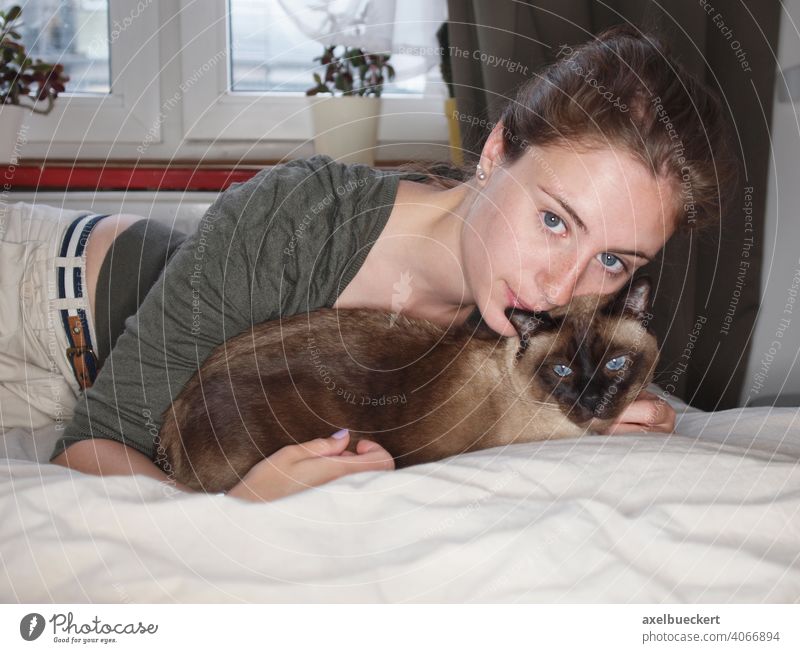 Junge Frau kuschelt mit Siamkatze auf dem Bett Katze Kater kuscheln schmusen Tierliebe Katzenbesitzer liegen Lifestyle Schlafzimmer gemütlich Erholung zu Hause