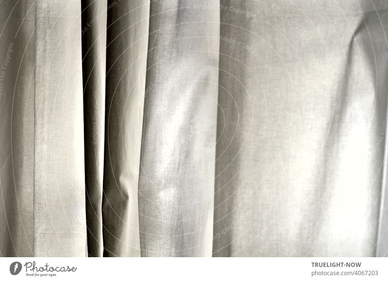 Ein Vorhang aus einfacher weisser Baumwolle hängt in senkrechten Falten und zeigt so eine Vielfalt an fein abgestuften Grautönen Stoff schwarz grau Abstufung