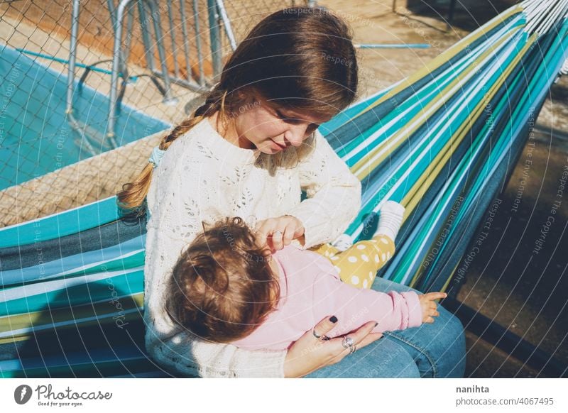 Junge Frau, die ihr Baby auf einer Hängematte sitzend pflegt Mama Familie Feiertage Pflege Liebe heimwärts im Freien Tagespflege Pool Umarmung tagsüber Routine