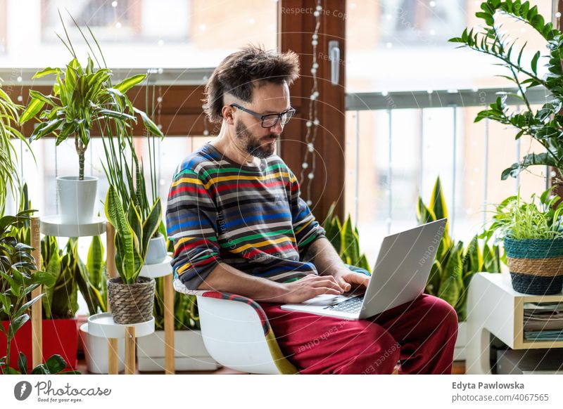 Junger Mann arbeitet zu Hause mit Laptop umgeben von Zimmerpflanzen online Onlinebanking Online-Lernen Online-Shopping Büro heimwärts Hand freiberuflich Mobile