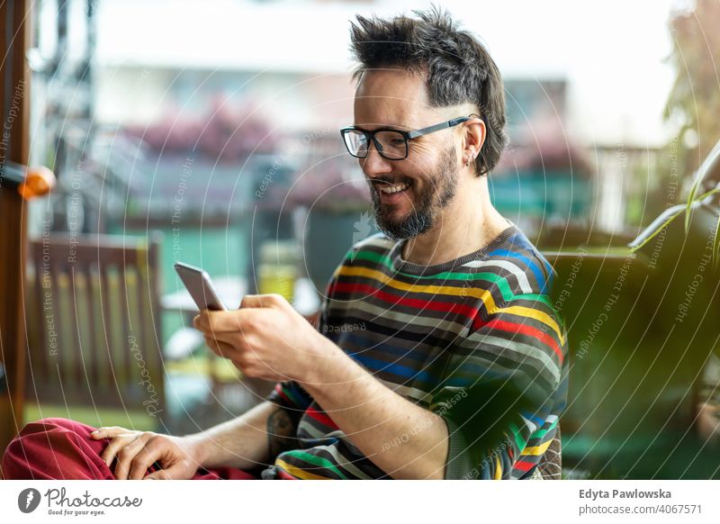 Glücklicher Mann, der ein Mobiltelefon zu Hause benutzt Arbeit Freiberufler Blogger Typ Anruf Texten online Kaukasier elektronisch Netzwerk digital Kunde
