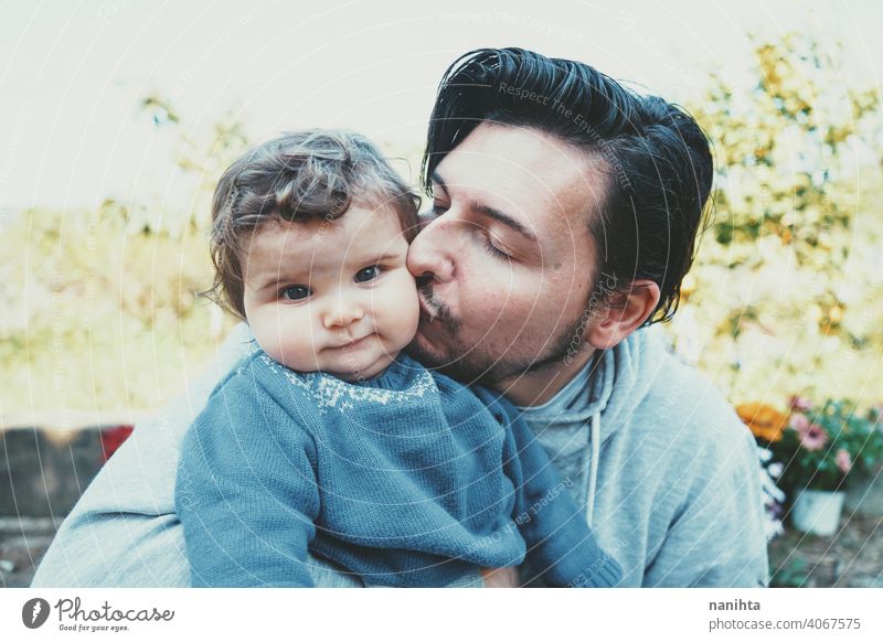 Junger Vater genießt einen sonnigen Tag mit seinem Baby im Garten Papa Familie Liebe Fröhlichkeit Kuss Pflege fürsorglich Kindererziehung lieblich niedlich