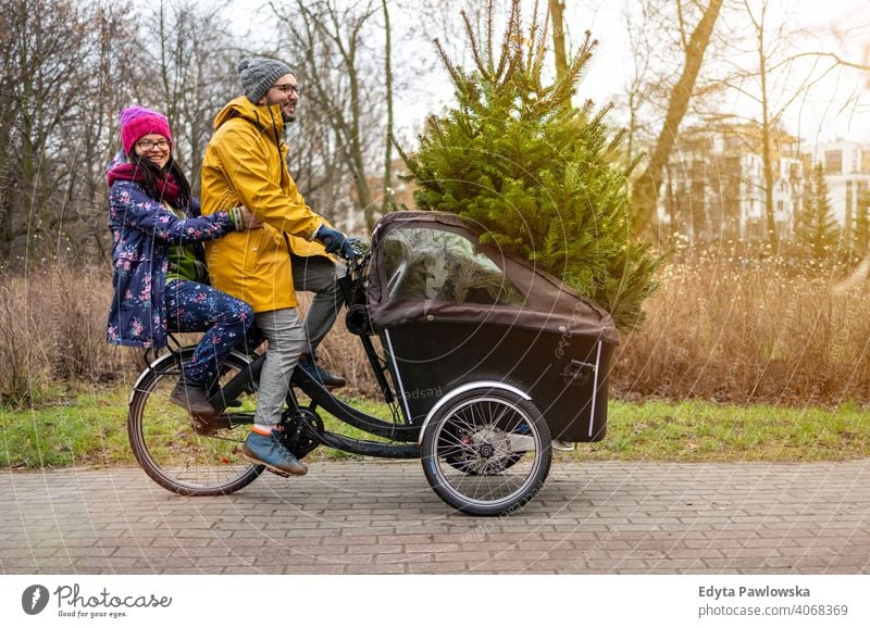Paar hat eine Fahrt mit Fracht Fahrrad transportieren Weihnachtsbaum nachhaltiger Transport Baum Spaß Freude genießend Hipster modern transportierend tragen