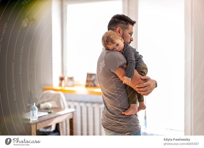 Papa legt Baby in seinen Armen zu Hause schlafen alleinerziehend alleinerziehender Vater Vatertag Vaterschaft zu Hause bleiben Dad Vaterschaftsurlaub