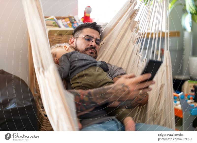 Mann überprüft sein Telefon, während sein kleiner Babysohn schläft alleinerziehend alleinerziehender Vater Vatertag Vaterschaft zu Hause bleiben Dad