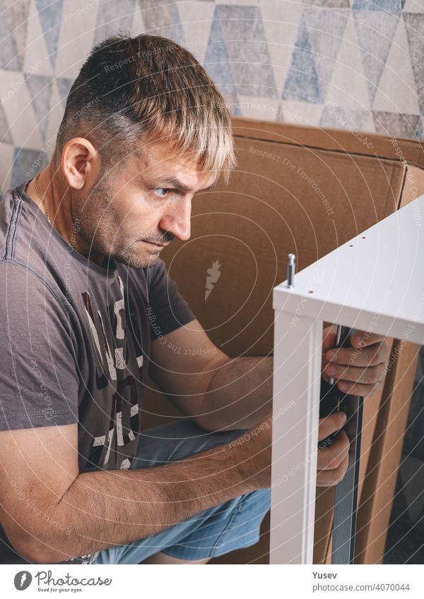 Mann beim Zusammenbau von Möbeln mit einem Schraubenzieher. Hausarbeit. Vorderansicht. Vertikale Aufnahme. Nahaufnahme Beteiligung Schraubendreher Arbeit