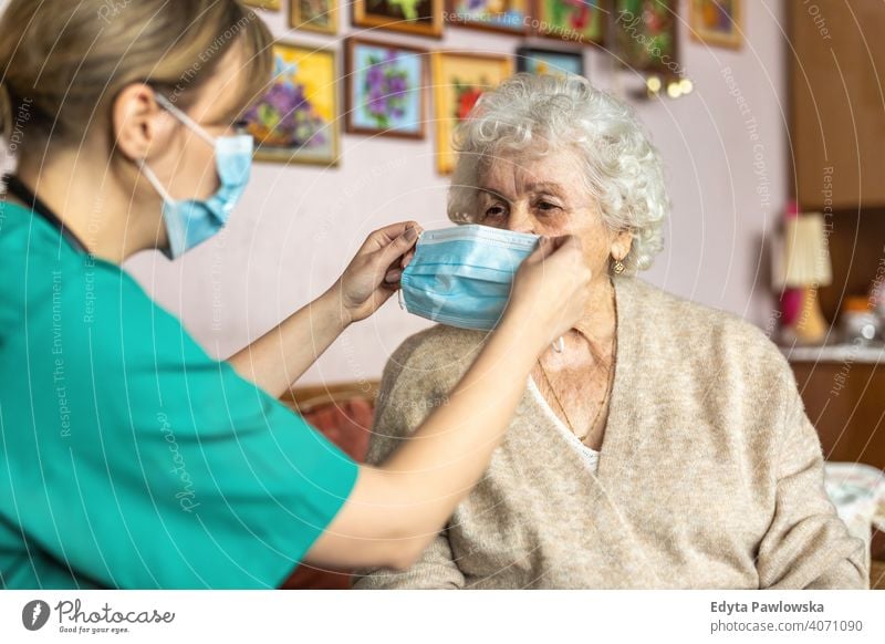 Krankenschwester hilft einer älteren Frau beim Anlegen der Gesichtsschutzmaske während eines Hausbesuchs Coronavirus Gesichtsmaske echte Menschen COVID Senior