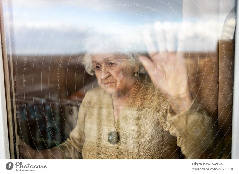 Ältere Frau schaut aus dem Fenster zu Hause COVID Sperrung Coronavirus Blick Quarantäne Blick durch das Fenster soziale Distanzierung Glas verwundbar Virus