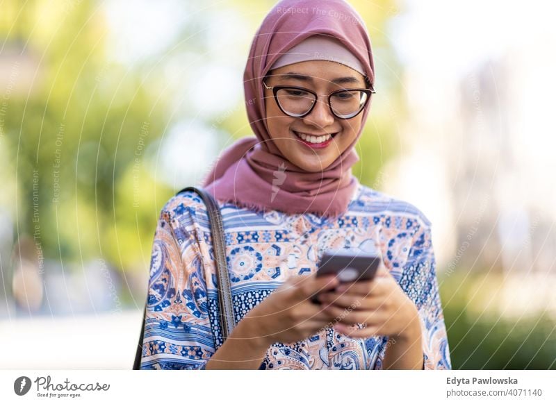 Lächelnde junge muslimische Frau mit Handy im Freien Hijab Kopftuch Islam arabisch Sommer Mädchen Menschen junger Erwachsener Lifestyle aktiv tausendjährig