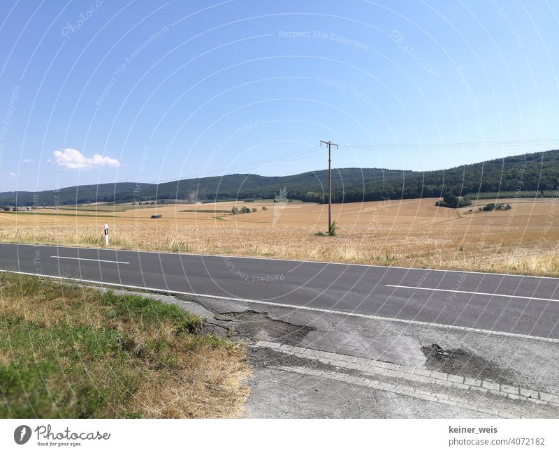 Straßenschäden im Hitzesommer und wüstes Ackerland nach der Ernte Landschaft Ackerbau ländlich Feld Asphalt Mittelstreifen Landstraße niergendwo Bauernhof