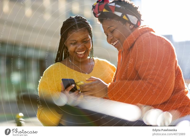 Glückliche Freundinnen, die mit ihren Smartphones in der Stadt Nachrichten versenden Vielfalt unterschiedliche Menschen Liebe im Freien Tag Positivität