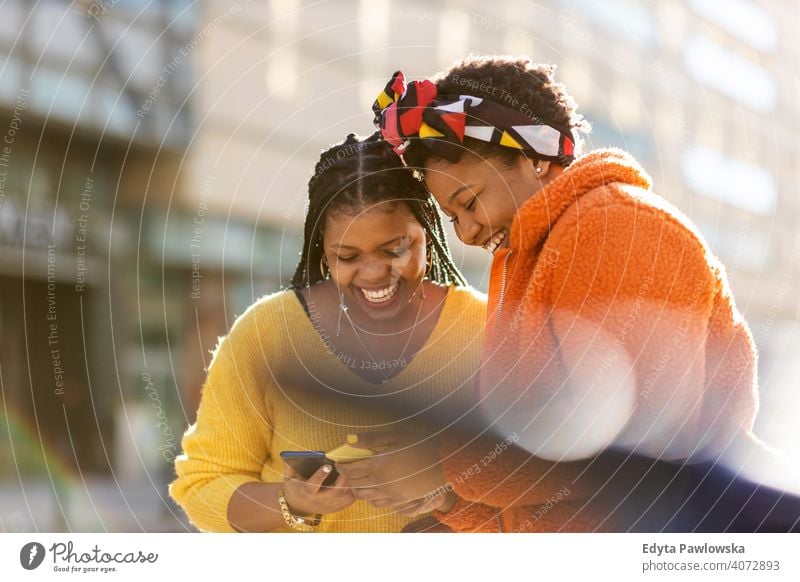 Glückliche Freundinnen, die mit ihren Smartphones in der Stadt Nachrichten versenden Vielfalt unterschiedliche Menschen Liebe im Freien Tag Positivität