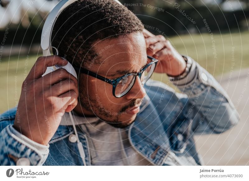 schwarzer Junge im Park, der mit Kopfhörern Musik hört Afro-Look Beteiligung Jugend trendy Teenager Freizeitkleidung Schlittschuh jung Porträt Sonnenuntergang