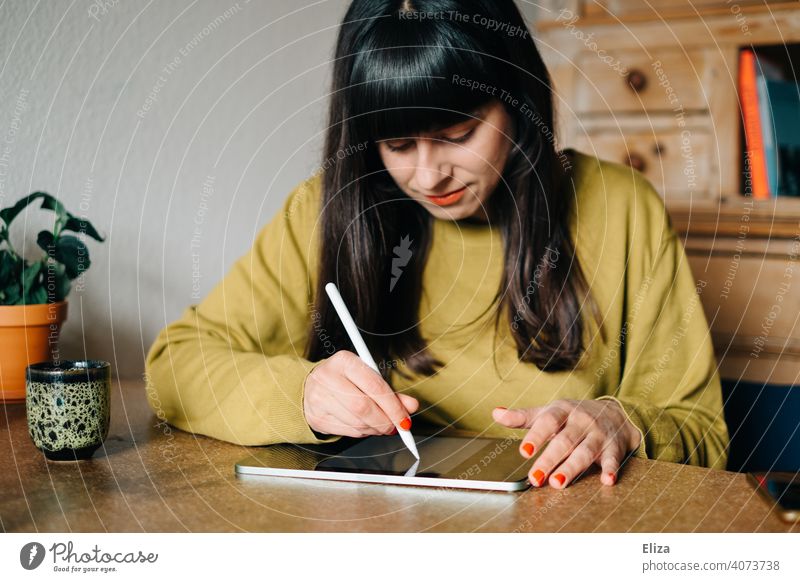 Eine Frau sitzt am Tisch und zeichnet oder schreibt etwas auf einem Tablet malen schreiben zeichnen Stift ipad Apple Pen Kreativität digital Grafikerin