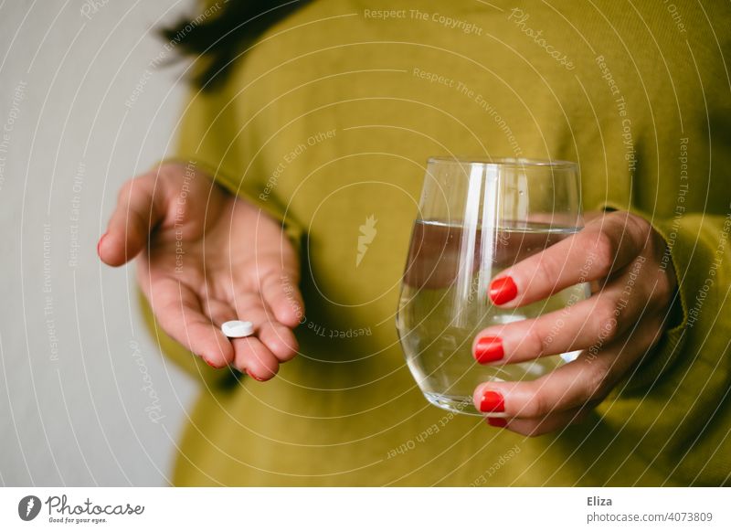 Eine Frau hält eine Tablette und ein Wasserglas in den Händen. Medikament einnehmen. Kopfschmerztablette Ibuprofen Gesundheit Krankheit Schmerztablette
