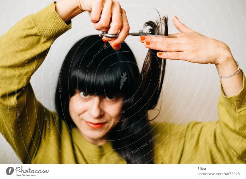 Eine braunhaarige Frau schneidet sich selber die Haare Haarschnitt schneiden Haare schneiden selber machen zuhause dunkelhaarig nachschneiden Lockdown DIY