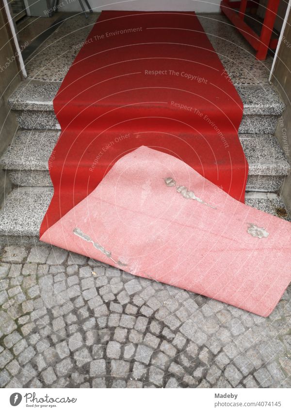Roter verwehter Teppich auf alten grauen Treppenstufen und grauem Kopfsteinplflaster am Eingang eines Friseur in der Altstadt von Oerlinghausen bei Bielefeld am Hermannsweg im Teutoburger Wald in Ostwestfalen-Lippe