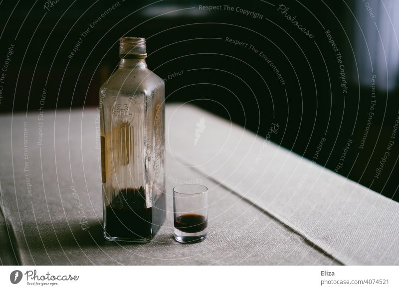 Schnapsflasche gefüllt mit Alkohol steht neben Schnapsglas auf einem Tisch Flasche trinken Alkoholsucht hochprozentig Einsamkeit Spirituosen Rauschmittel