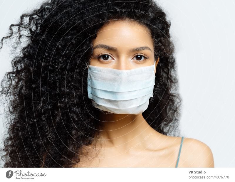 Ernste afroamerikanische Frau versucht, Virus und epidemische Krankheit zu stoppen, bleibt während des Ausbruchs der Infektion zu Hause, trägt medizinische Maske, isoliert auf weißem Hintergrund, wird ins Krankenhaus eingeliefert, diagnostiziert