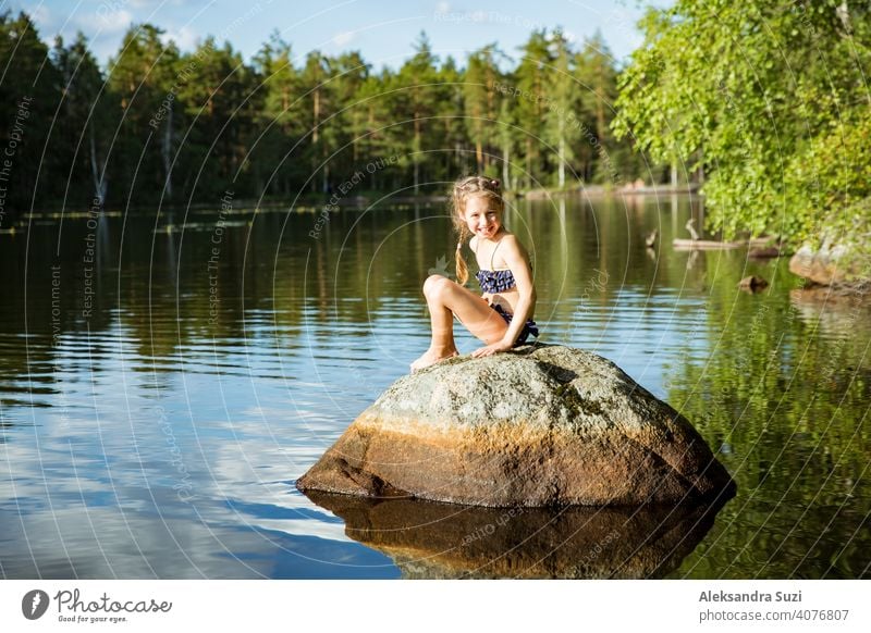 Nettes kleines Mädchen sitzt auf einem Felsen im See. Genießen Sie den Sommerurlaub. Kind und Natur. Glückliche Isolation Konzept. Finnland erforschen. Skandinavische Landschaft.