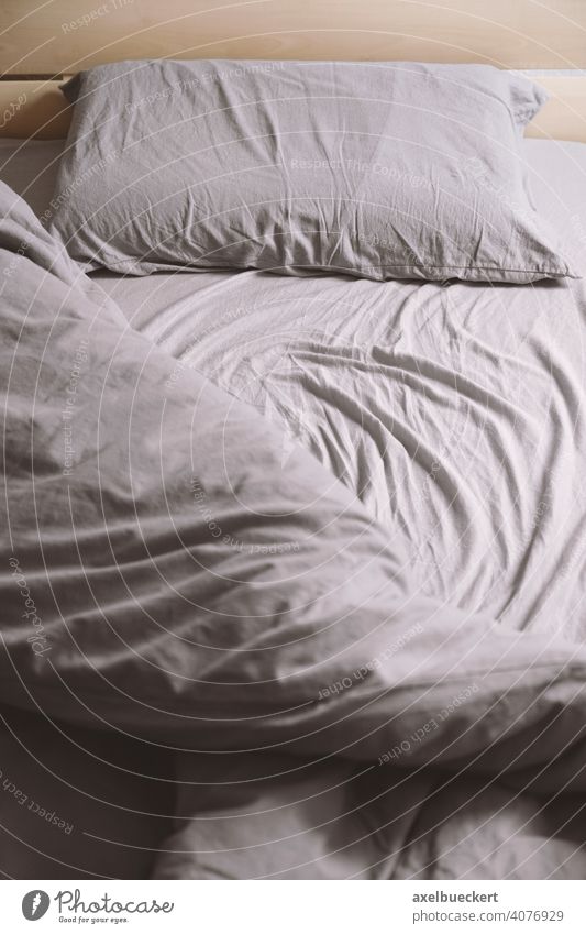 leeres ungemachtes Bett mit zerknittertem Laken oder Bettwäsche Einzelbett unordentlich Schlafzimmer Kopfkissen Morgen schlafen Möbel Bettdecke Tag grau