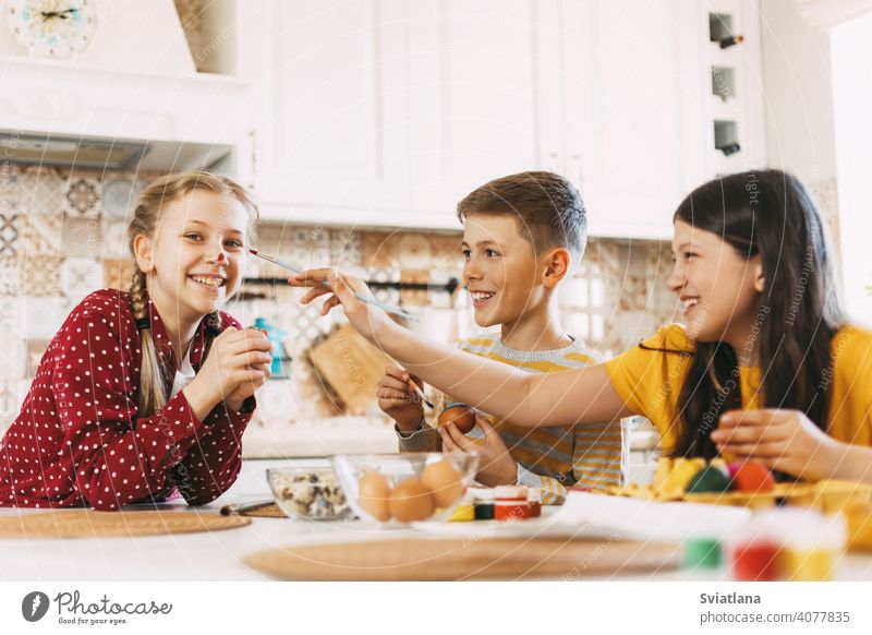 Zwei Schwestern und ein Bruder sitzen am Tisch und bemalen Ostereier in verschiedenen Farben für Ostern, lachen und schwelgen Frühling Kind Feiertag