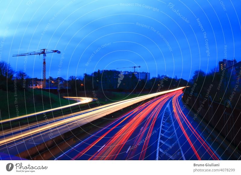 Leichte Spur von Autos auf einer Autobahn während des Morgens. Geschleuderte Fahrzeuge auf der Straße, gesehen von einer Brücke. Lightpainting-Szene. Gebäude