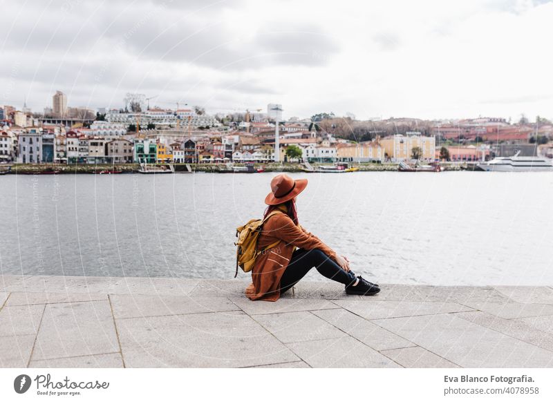 Rückenansicht der jungen schönen Frau sitzt am Fluss bei Sonnenuntergang genießen Porto Ansichten. Reisen Konzept reisen Großstadt Sightseeing urban Kaukasier