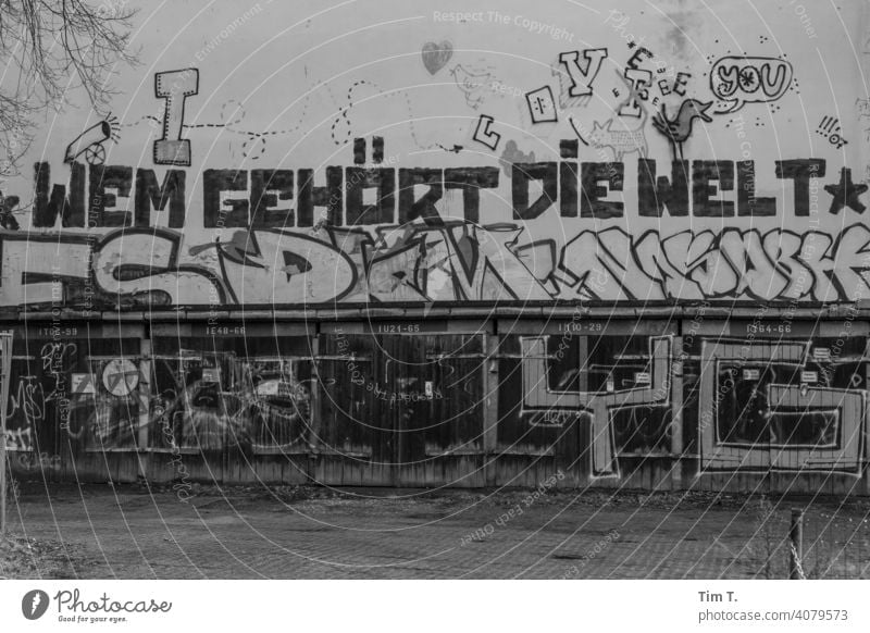 ein Graffiti auf der Fassade über den Garagen "Wem gehört die Welt" Weißensee Berlin Garagentor old Menschenleer Außenaufnahme Wand Einfahrt Tag Tor Gebäude